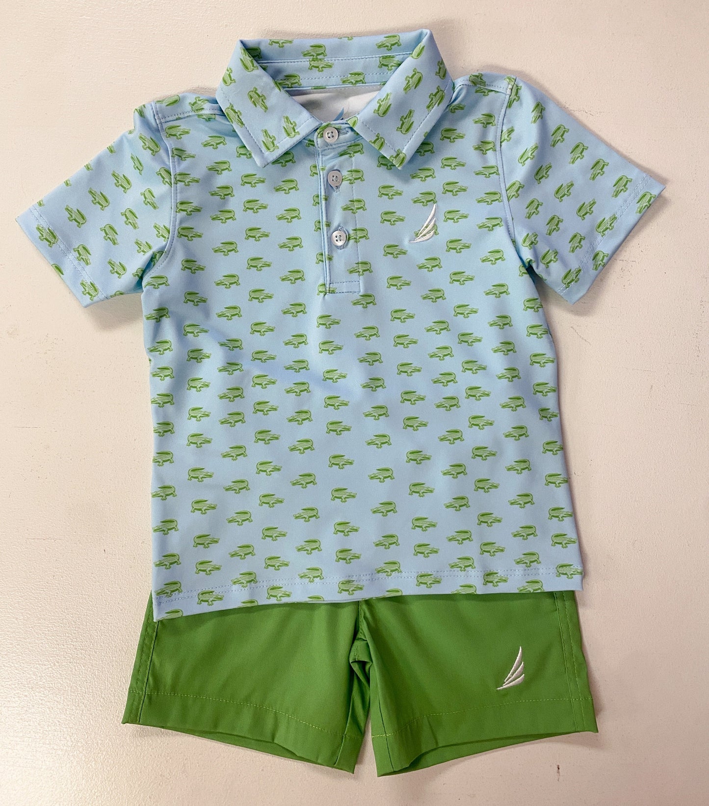 Children's blue polo shirt with green car pattern and green shorts on a beige background