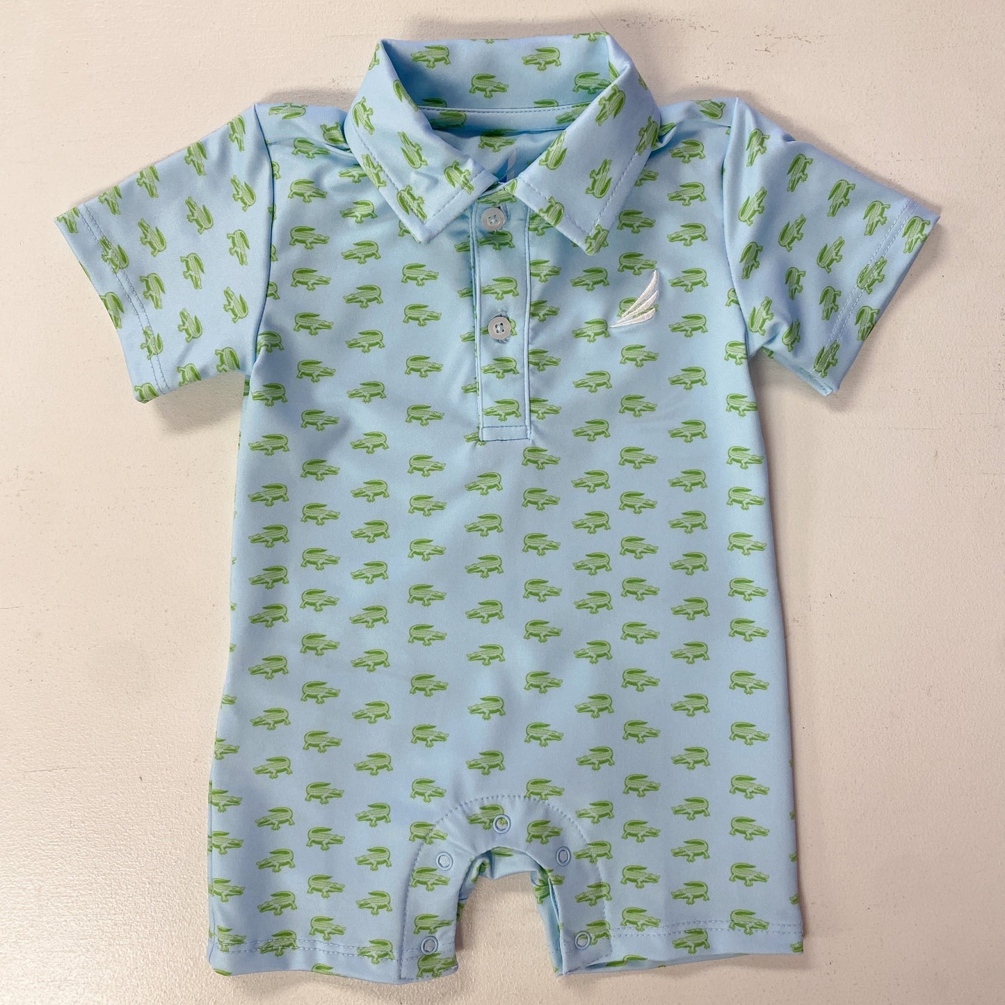 Baby romper with green alligator pattern on a beige background